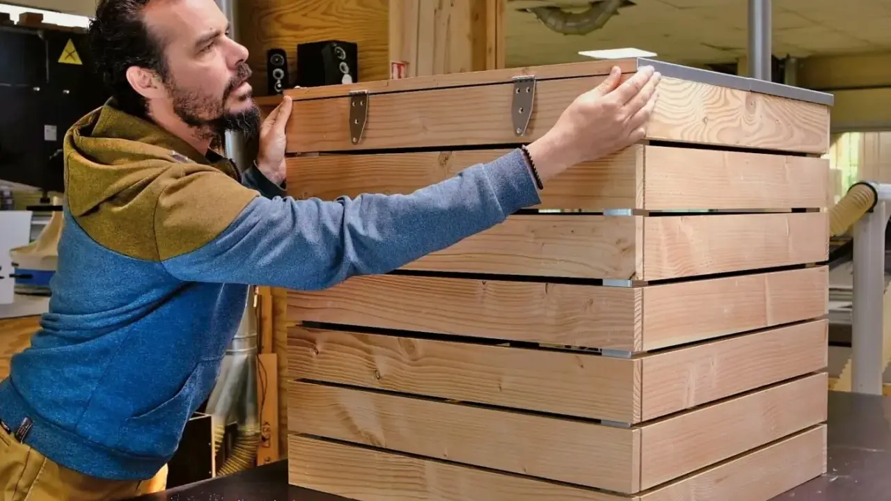 Un homme assemble des planches de bois pour fabriquer un composteur.
