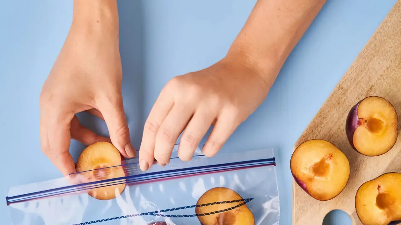 Mains mains placent des moitiés de prunes coupées dans un sac de congélation pour congeler des prunes.