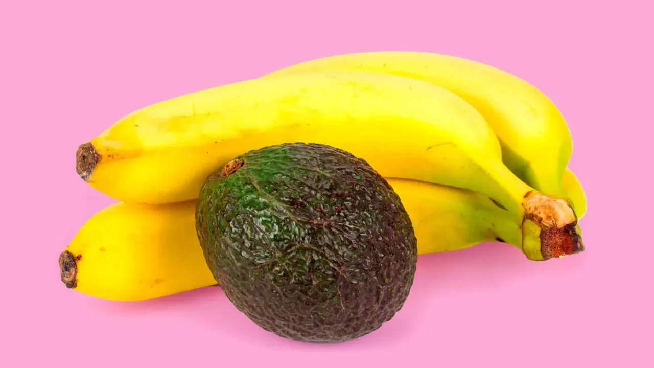Un avocat vert foncé repose à côté d'une grappe de bananes jaunes mûres. La banane est connue pour aider à faire murir l'avocat.