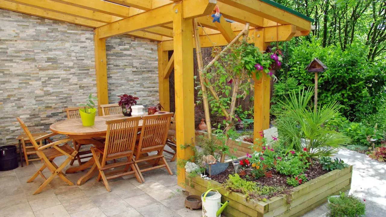 Une pergola en bois pour fabriquer une pergola pour plante grimpante, avec table et chaises, et un parterre de fleurs.