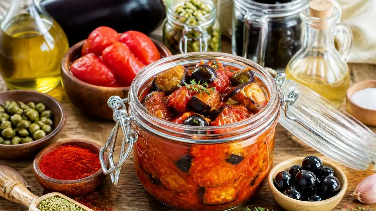 Un bocal de conserve d'aubergine au naturel, avec des tomates, des olives, des câpres et des épices.