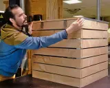 Un homme assemble des planches de bois pour fabriquer un composteur.