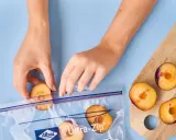 Mains mains placent des moitiés de prunes coupées dans un sac de congélation pour congeler des prunes.