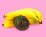 Un avocat vert foncé repose à côté d'une grappe de bananes jaunes mûres. La banane est connue pour aider à faire murir l'avocat.