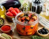 Un bocal de conserve d'aubergine au naturel, avec des tomates, des olives, des câpres et des épices.