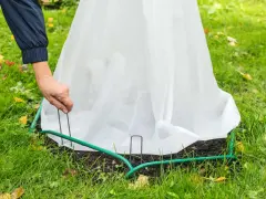 Une main ajuste un voile d'hivernage fait maison autour d'une plante pour la protéger du froid.