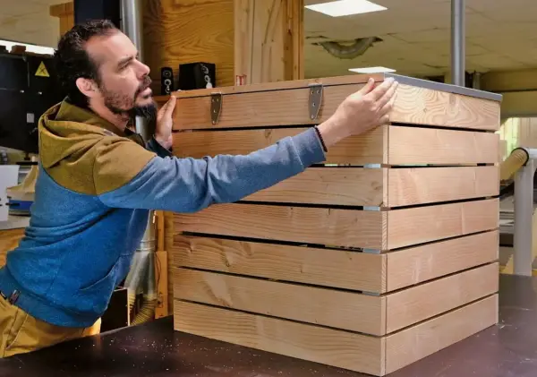 Un homme assemble des planches de bois pour fabriquer un composteur.