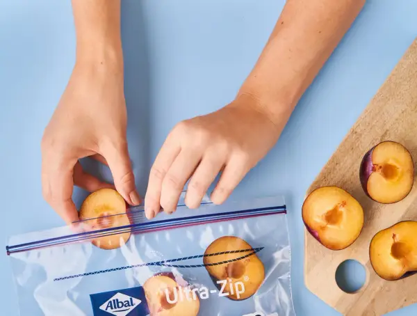 Mains mains placent des moitiés de prunes coupées dans un sac de congélation pour congeler des prunes.