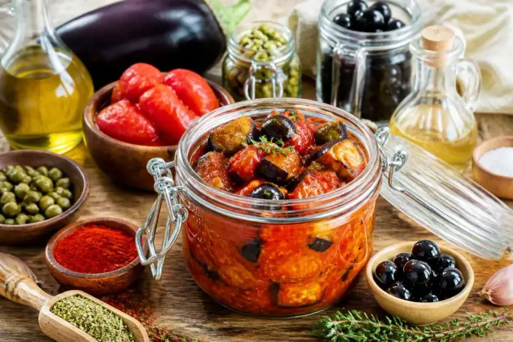 Un bocal de conserve d'aubergine au naturel, avec des tomates, des olives, des câpres et des épices.