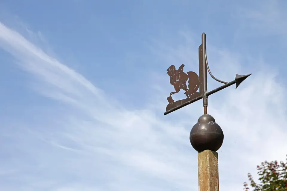 Girouette en forme de poussin sortant d'un œuf, indiquant le vent des rameaux sous un ciel bleu parsemé de nuages fins.
